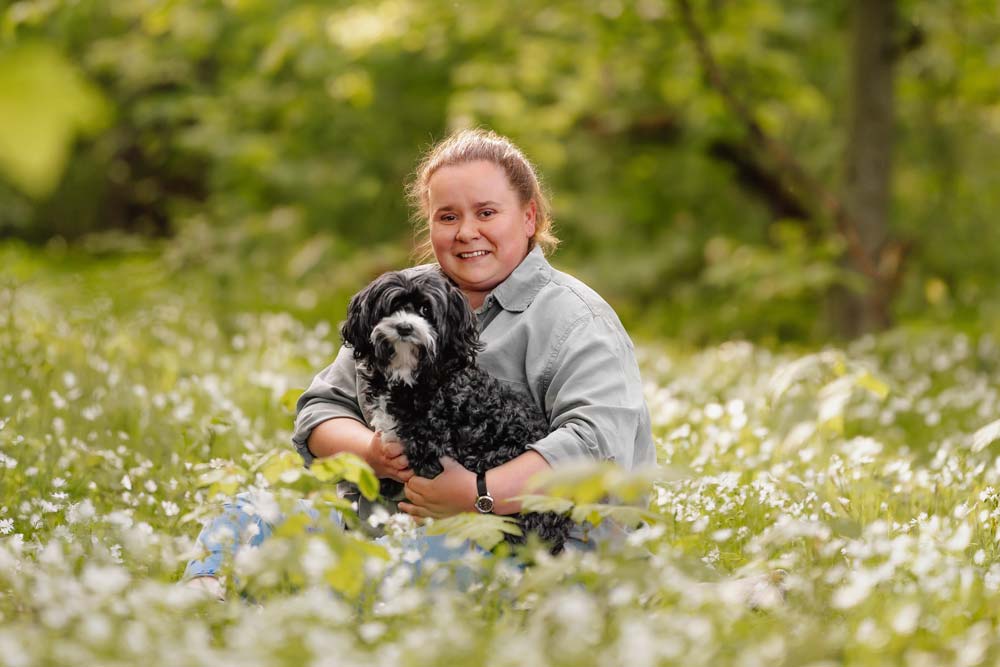 Praxisinhaberin Solveig Schnell sitzt in einer Wiese mit Hund